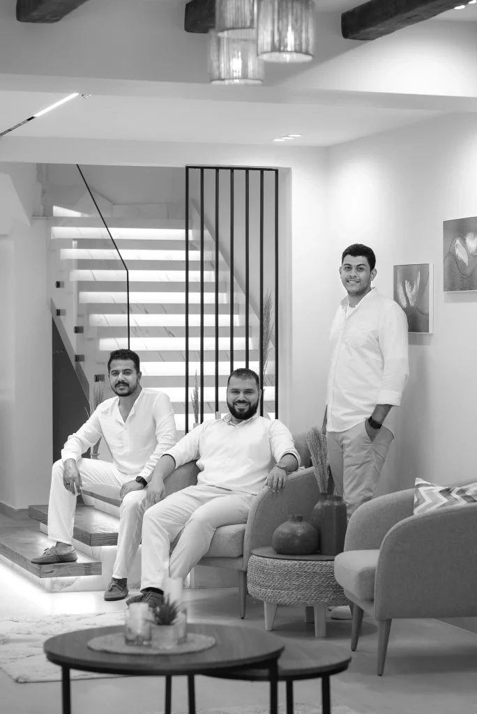 The three partners of AIM Architects in a living room, a lit staircase behind them.